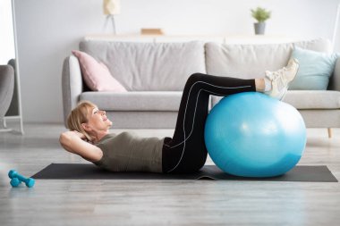 Olgun bir bayanın evde kaslarını yoga minderiyle çalıştırması, uzayı kopyalaması.