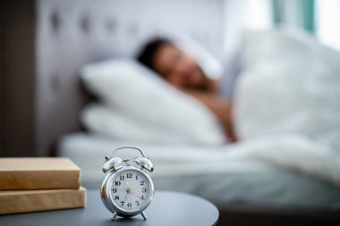 Erken uyanış konsepti. Sabahları çalar saatin başında uyuyan, yatakta yatan bir adam.