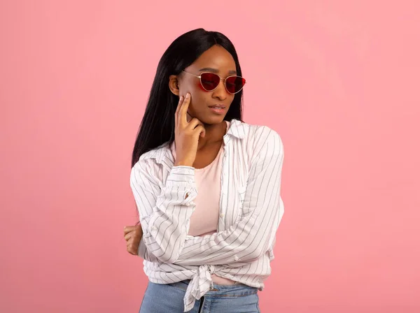 Portrait of cool African American woman in casual clothes and sunglasses on pink studio background