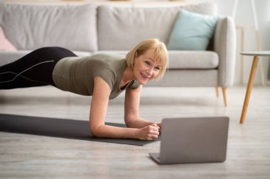 Çevrimiçi sporlar, tecrit sırasında. Evde dizüstü bilgisayarın önünde egzersiz yapan olgun bir kadın.