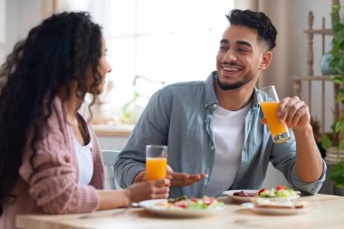 Neşeli bir Arap çifti, lezzetli kahvaltının tadını çıkarıyor ve mutfakta meyve suyu içiyor.