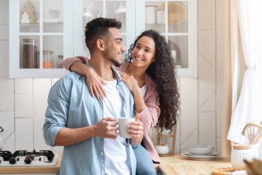 Mutlu genç Arap eşler, sıcak mutfağın içinde kahve içip sarılıyorlar.