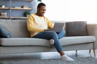 Siyah adam evde dizüstü bilgisayar kullanarak vakit geçiriyor.