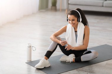 Fitness minderinde dinlenip müzik dinleyen mutlu genç bir kadın.