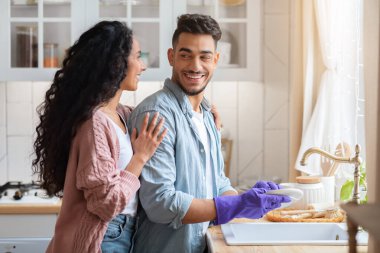 Mutfakta bulaşık yıkarken kocasını kucaklayan bir Arap kadını sevmek.