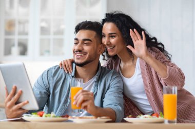 Modern Müslüman çift mutfaktaki dijital tablette video çağrısı yapıyor.