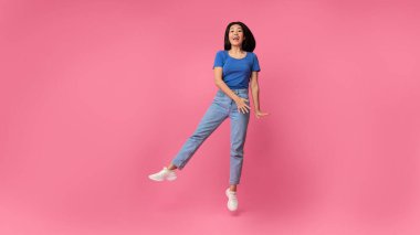 Pembe stüdyoda zıplayan mutlu Asyalı genç bayan.