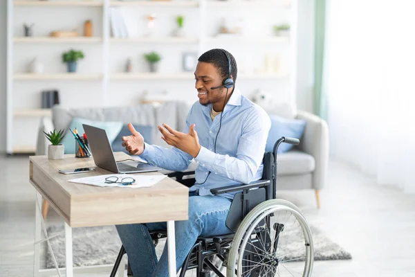 Niepełnosprawny czarny facet z słuchawkami komunikujący się online na laptopie, mający spotkanie biznesowe z domu — Zdjęcie stockowe