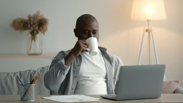 Africano homem no laptop tendo café trabalhando sentado em casa — Vídeo de Stock