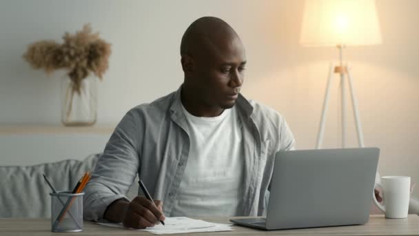 Afrykanin robi notatki o kawę siedzi na laptopie w domu — Wideo stockowe