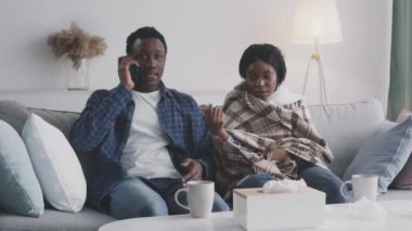 Siyahi bir koca cep telefonuyla doktoru arıyor, hasta karısının sıcaklığını söylüyor, evde otobüsün üstünde oturuyor.