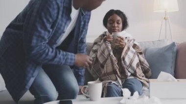 Hasta karısına bitki çayı getiren Afrikalı Amerikalı koca. Ekoseye sarılmış minnettar kadın.