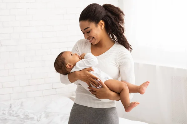 Svart mamma håller baby i armarna stående i sovrummet inomhus — Stockfoto