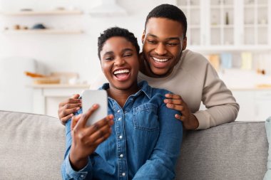 Kanepede oturan Afro-Amerikan çift akıllı telefon kullanıyor.