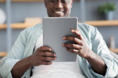 Boş zaman kavramı. Siyah adam dijital tablet kullanıyor, haberleri okuyor ya da internette geziniyor, evdeki kanepede dinleniyor.