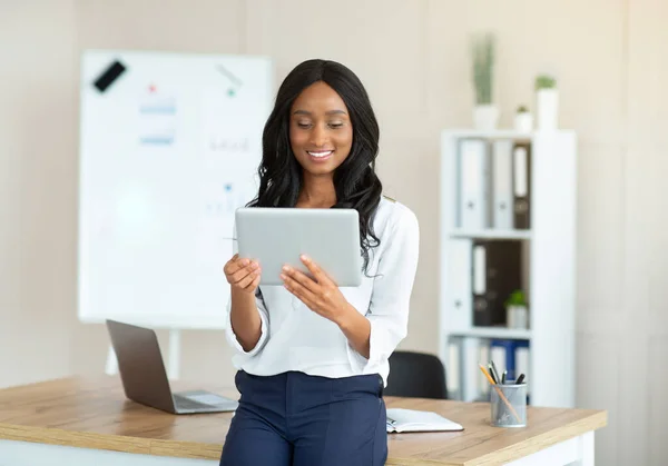 Remote work concept. Joyful black lady using tablet pc, searching info on web at modern office