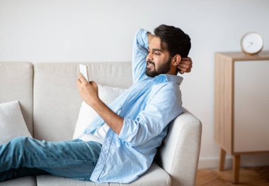 Milenyum doğulu adam akıllı telefonuyla kanepede dinleniyor, internette geziniyor.