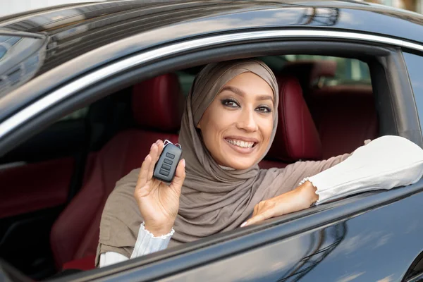 Muslim lady showing auto keys, sitting on drivers seat