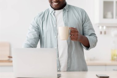 Mutfakta dizüstü bilgisayar kullanan, çay içen, sosyal medyada gezinen ya da internet haberleri okuyan tanınmamış siyahi bir adam.