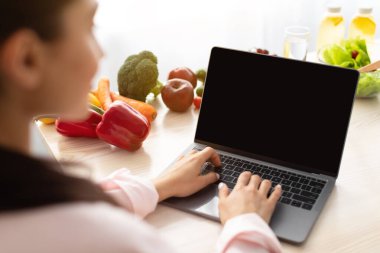 Mutfakta boş ekranlı dizüstü bilgisayar kullanan bir kadın.