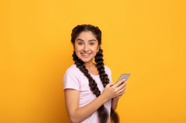 Sarı arka planda izole edilmiş akıllı telefon kullanan Hintli kadın.