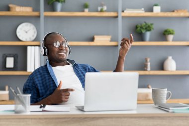 İşte mola. Neşeli siyah adam kulaklıkla müzik dinliyor ve iş yerinde sanal gitar çalıyor.
