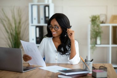 Çağdaş ofisteki masasında evrak okuyan profesyonel bayan yöneticinin portresi.