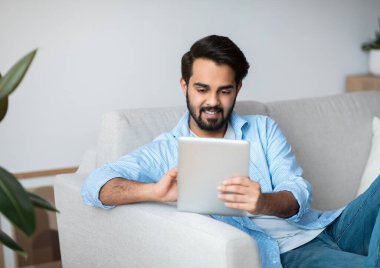 Yakışıklı Doğulu adam evde dinlenirken dijital tablette interneti tarıyor.