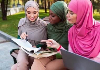 Üç Müslüman kız öğrenci birlikte öğreniyor. Dışarıda bankta oturuyorlar.