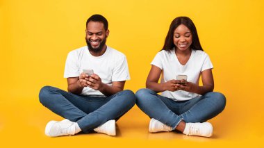 Stüdyoda yerde oturan akıllı telefon kullanan siyah bir çift.