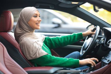 Gülümseyen Müslüman kadın şehir merkezinde yeni araba sürme denemesi yapıyor.