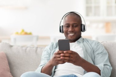 Müziğin tadını çıkar. Cep telefonlu, kulaklıklı, internette sörf yapan mutlu siyahi adam.