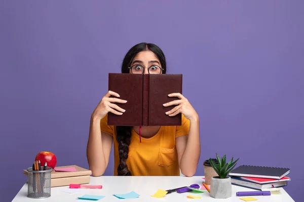 Zszokowana kobieta w okularach chowa się za książką, podgląda — Zdjęcie stockowe
