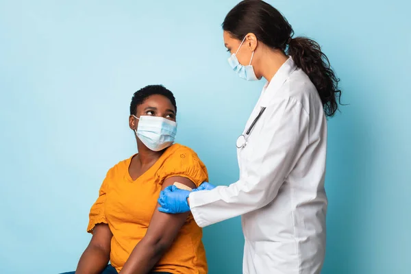 Travailleur médical vaccinant la femme noire portant des masques faciaux, fond bleu — Photo