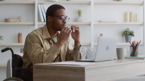 Hombre discapacitado cansado en silla de ruedas en el ordenador portátil frotando los ojos en interiores — Vídeos de Stock