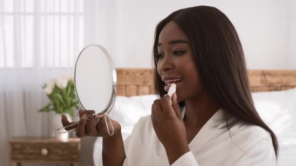 Αφρικανή γυναίκα που εφαρμόζει κραγιόν ή lips balm κάνοντας μακιγιάζ σε εσωτερικούς χώρους — Αρχείο Βίντεο