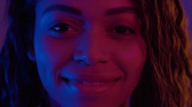 Neon ışıklarıyla kameraya gülümseyen mutlu Afro-Amerikan genç bayan portresi