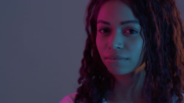 Femme afro-américaine ludique tournant visage à caméra et clignant des yeux joyeusement dans la lumière au néon, au ralenti — Video