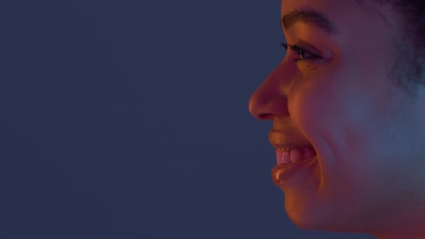 Profiel portret van jonge gelukkige Afro-Amerikaanse vrouw glimlachend en opzij kijkend naar kopieerruimte in neon lichten — Stockvideo