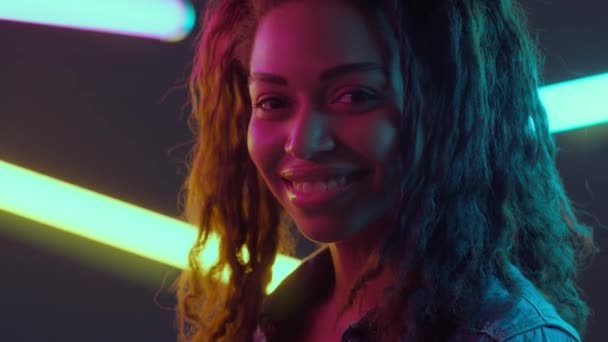 迷人的年轻的非洲姑娘坐在霓虹灯下，拿着点着的灯在俱乐部的墙上摆姿势 — 图库视频影像