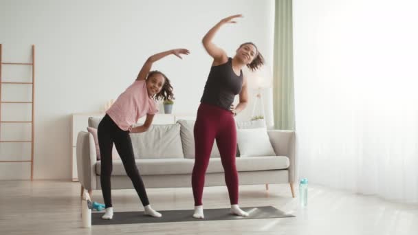 Šťastný africký americký matka a dcera cvičení společně doma, naklánění těla na stranu, zpomalení — Stock video
