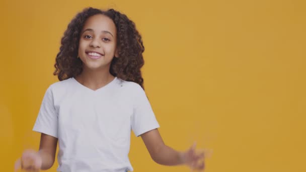 Mignon afro-américain adolescent fille pointant de côté et souriant, fond de studio orange avec un espace vide pour la maquette — Video