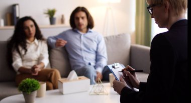 Kadın psikoterapist notlar alıyor, danışma sırasında ilişki sorunları yaşayan genç eşlere teşhis koyuyor