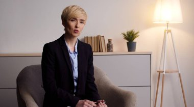 Yaşam koçluğu. Kendinden emin orta yaşlı bir bayan kamerayla konuşuyor, ofiste video dersi kaydediyor.