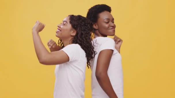 Dos jóvenes afroamericanas felices bailando, divirtiéndose juntas, paradas espalda con espalda, fondo naranja, — Vídeo de stock