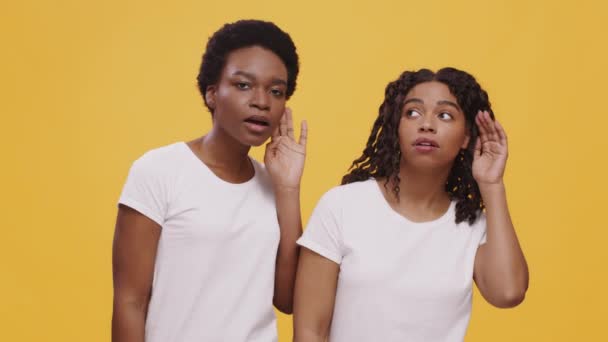 Due curiose amiche afroamericane che ascoltano a parte, si tengono per mano vicino alle orecchie e cercano di sentire segreti — Video Stock