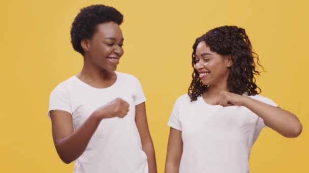 Trabalho de equipa feminino e amizade. Duas mulheres afro-americanas fazendo gesto punho colisão e rindo, fundo laranja, — Vídeo de Stock