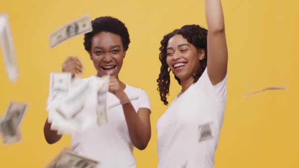 Two excited african american women dancing under money shower, enjoying successful deal, orange background — Stock Video