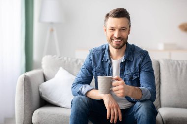 Oturma odasında kahve içen yakışıklı bir adam.