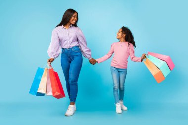 Afro-Amerikalı kadın ve kız alışveriş torbalarıyla yürüyorlar.